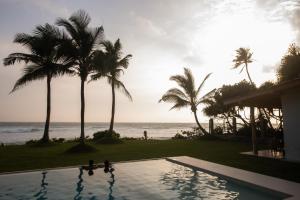 a swimming pool in front of the ocean with palm trees at Swell Shacks in Matara