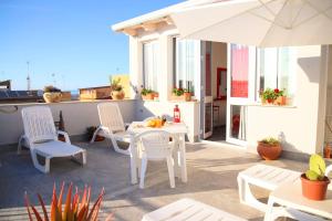 d'une terrasse avec des tables et des chaises blanches et un parasol. dans l'établissement Appartamento L'airone Balestrate, à Balestrate