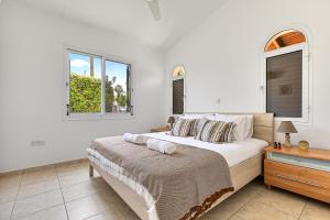 a white bedroom with a bed and two windows at Coral Bay Avenue Villa by Vichy Holidays in Paphos