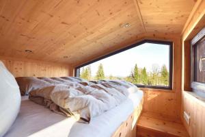 a bed in a wooden room with a large window at SEINZ Tiny House Natururlaub in Bad Kohlgrub