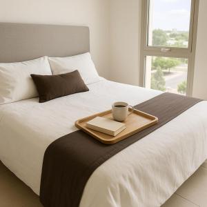a tray with a cup and a book on a bed at NUEVO Puerto Norte con cochera opcional in Rosario