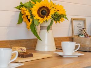 Un jarrón lleno de girasoles sobre una mesa con dos tazas. en Cwmporthman Farm Cwtch-Uk34700, en Blaenporth
