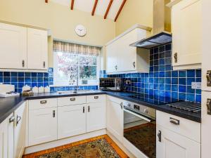 a kitchen with white cabinets and blue tiles at Ysgubor - Uk31389 in Caeathro