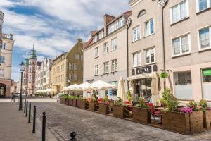 a street with buildings and tables with flowers and umbrellas at Holy Spirit Street Apartments in Gdańsk