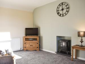 ein Wohnzimmer mit einem TV und einer Uhr an der Wand in der Unterkunft Benwells Holiday Cottage in Maud