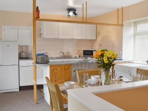 eine Küche mit weißen Schränken und einem Tisch mit Blumen darauf in der Unterkunft The White Cottage in Furness Vale