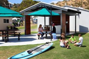 eine Gruppe von Menschen, die mit einem Surfbrett auf dem Gras sitzen in der Unterkunft Brighton Beachfront Holiday Park Adelaide in Brighton