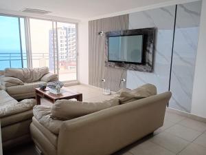 a living room with two couches and a television on a wall at Penthouse frente al mar in Tonsupa