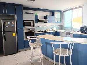a kitchen with blue cabinets and two bar stools at Penthouse frente al mar in Tonsupa