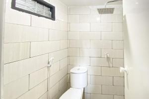 a white tiled bathroom with a toilet and a window at RedDoorz Yasmine Syariah near Taman Dayu in Jetak +18 photos