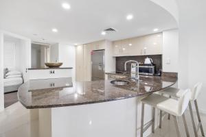a kitchen with a counter with a sink and chairs at Zanzibar 404, Sensational 2 Bedroom Oceanview Apartment in Mooloolaba