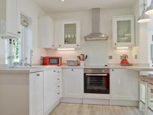 a white kitchen with white cabinets and a red appliance at Wishing Well Cottage in Mathon