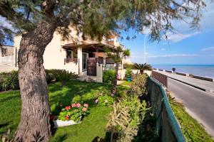a house on the beach with a tree and flowers at Terrazza a mare Corallo in Marina di Ragusa +12 photos