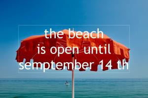 a red umbrella on the beach with the words the beach is open until seventh at Hotel Riviera & Maximilian's in Trieste