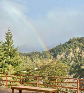 Un arcoíris sobre una montaña con un banco de madera. en Cabaña De Montaña Ámber II, en San Carlos de Bariloche