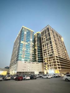 アジュマーンにあるAppartement 1BR de 2024 avec piscine et salle de sportの駐車場に車を停めた高層ビル2棟