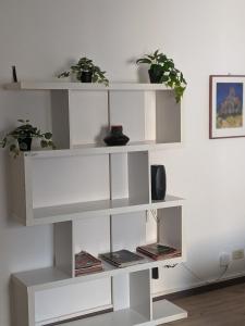 a white book shelf with two potted plants on it at In the center of Modena, Piazza Roma and the Ferrari Museum in Modena