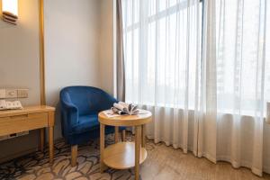 Zimmer mit einem blauen Stuhl, einem Tisch und einem Fenster in der Unterkunft Vienna Hotel Fuzhou Mawei Banzheng Cultural Scenic Area Branch in Fuzhou