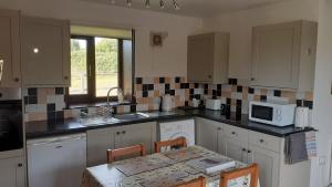 a kitchen with white cabinets and a table with a microwave at Paddock Bungalow in Mundesley +19 photos