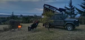 une personne assise sur une chaise à côté d'une jeep dans l'établissement Camping Near Mt Longonot, Elwai Camping Centre, à Heni Village