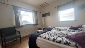 a bedroom with a bed and a chair and two windows at Kirkjufell Guesthouse and Apartments in Grundarfjordur