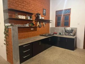 a kitchen with black cabinets and a brick wall at Mahiyanganaya Holiday Resort in Mahiyangana
