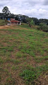 a field of grass with a house in the background at Camping Caldeirão Furado in São Thomé das Letras