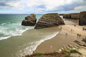 Eine Gruppe von Menschen, die an einem Strand mit großen Felsen spazieren gehen in der Unterkunft Oasis o,xuncal in San Cosme de Barreiros