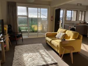 a living room with a yellow couch and a white rug at Spacious Studio - Self Contained in Tauranga