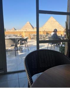 Una persona sentada en una mesa mirando por una ventana las pirámides. en Sena pyramids view inn, en El Cairo