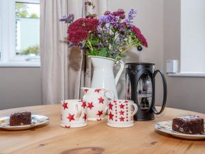 une table avec des tasses à café et un vase avec des fleurs dans l'établissement Wren Cottage, à Sutton