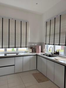 a kitchen with white cabinets and windows with shutters at Casa Anggeriani in Jitra