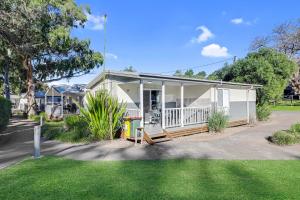 a small white house with a porch and a yard at Kendalls Beach Holiday Park in Kiama