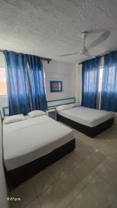 2 Betten in einem Zimmer mit blauen Vorhängen in der Unterkunft LUUM hotel acapulco in Acapulco