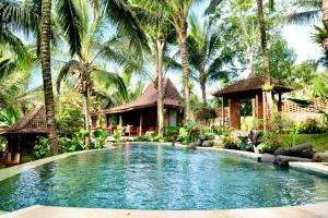 a swimming pool in front of a house with palm trees at The Manikyang Residence in Tabanan