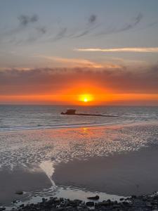 a sunset on a beach with the sun setting at L'Heurt Bleue - Maison de pêcheur face mer in Le Portel