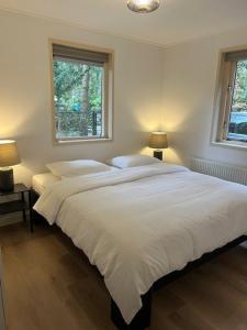 a bedroom with a large white bed with two windows at Forest house with sauna in Norg