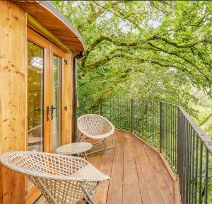 a wooden deck with two chairs and a table at Treehouse In Devon - riverside woodland hideaway in Beaworthy