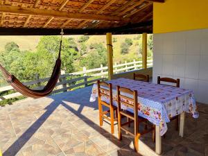 a table and chairs on a porch with a hammock at Sitio Boa Esperança II - 20km de Monte Verde in Camanducaia