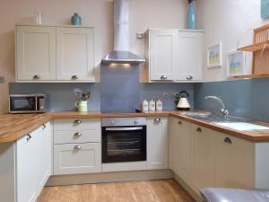 eine Küche mit weißen Schränken und einem Herd in der Unterkunft Old Rectory Cottage - Dinas Country Club in Dinas