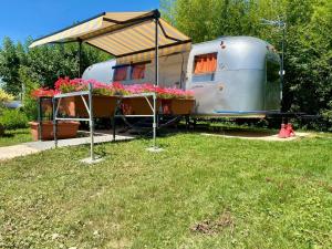 a trailer with a roof and flowers in a yard at Le Clos de Tanvol - Parking privé GRATUIT- Terrasse Privée - Climatisation - Caravane Airstream in Viriat