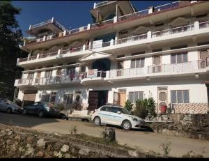 a large white building with cars parked in front of it at Kedar palace in Ukhimath