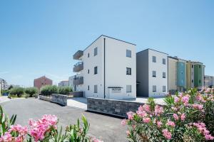 two white buildings in a parking lot with pink flowers at ColorsVibe Apartment in Trogir