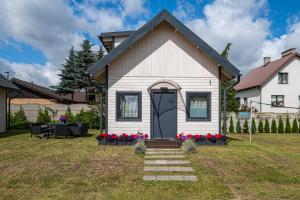 Una pequeña casa blanca con una puerta negra y flores rojas. en Domki Bukowy Las, en Rewa
