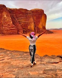 een vrouw die op een rots staat voor een rotsformatie bij Wadi Rum Oday Luxury Camp in Wadi Rum