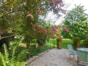 um pátio com uma mesa e cadeiras debaixo de uma árvore com flores cor-de-rosa em Les Chambres de la Nied em Condé-Northen