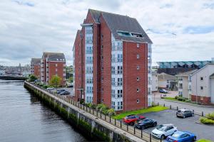 a tall red brick building next to a river at River Ayr View-Coorie Doon Stays in Ayr
