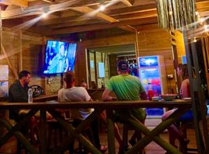 ヌキにあるHotel Meraki Nuquiのバーに座ってテレビを見ている人々のグループ