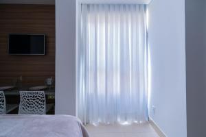 a bedroom with white curtains and a table and a television at Loft novo e aconchegante perto do centro histórico in São João del Rei +26 photos