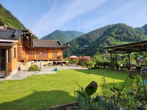 a house with a yard with mountains in the background at Danyang Gahyeonjeong Pension in Danyang